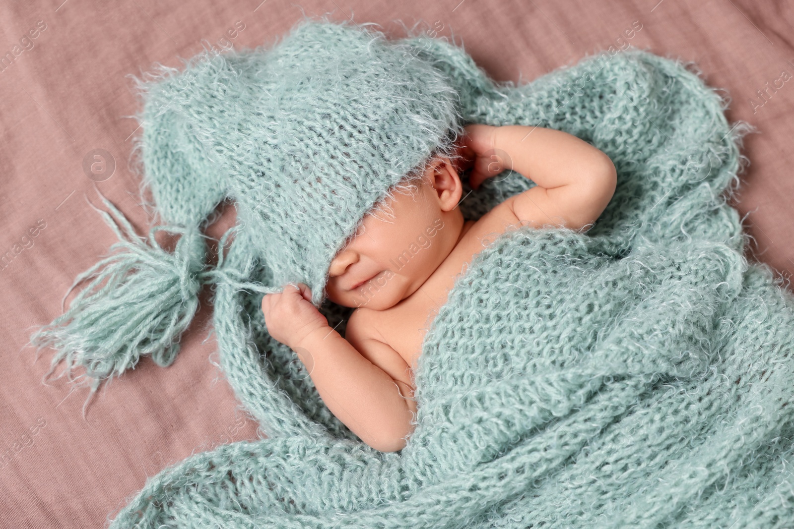 Photo of Adorable newborn baby sleeping under knitted plaid on bed, top view
