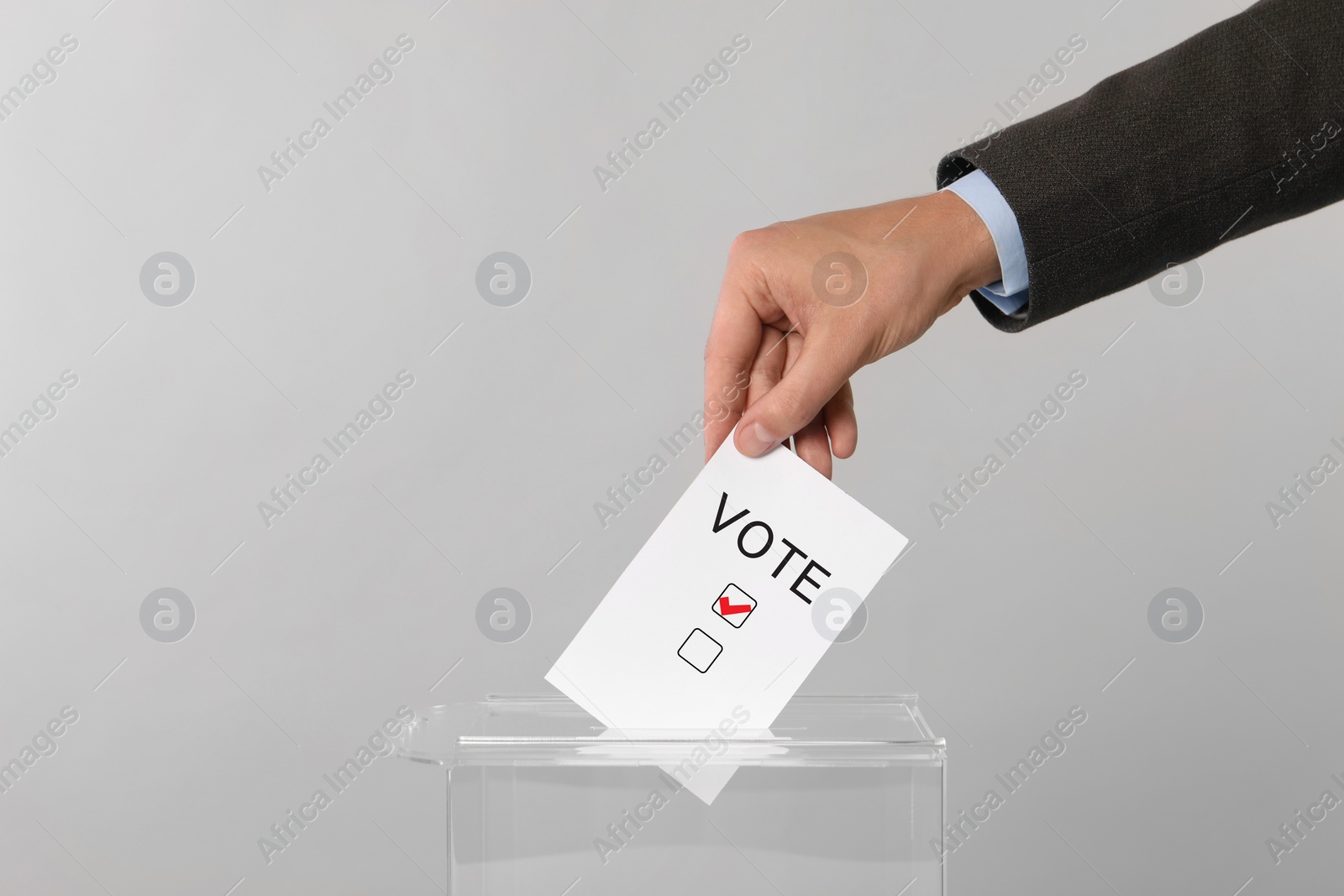 Image of Man putting paper with word Vote and tick into ballot box on light grey background