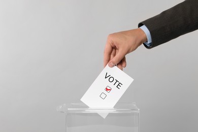 Man putting paper with word Vote and tick into ballot box on light grey background