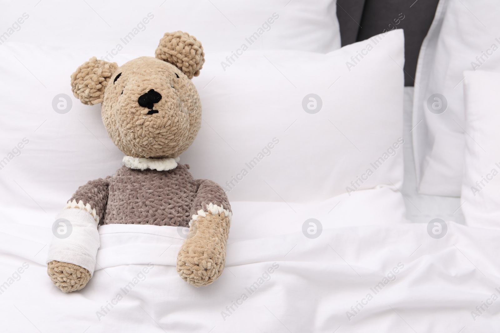 Photo of Toy cute bear with bandage under blanket in bed