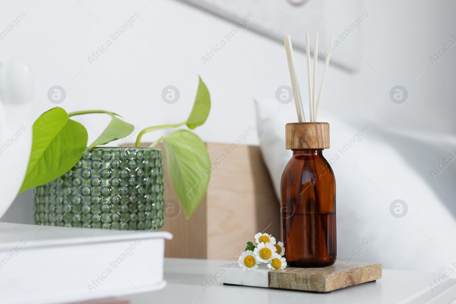 Photo of Aromatic reed air freshener, chamomiles and houseplant on white table in bedroom