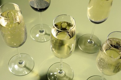 Photo of Many glasses of delicious sparkling wine on light yellow background