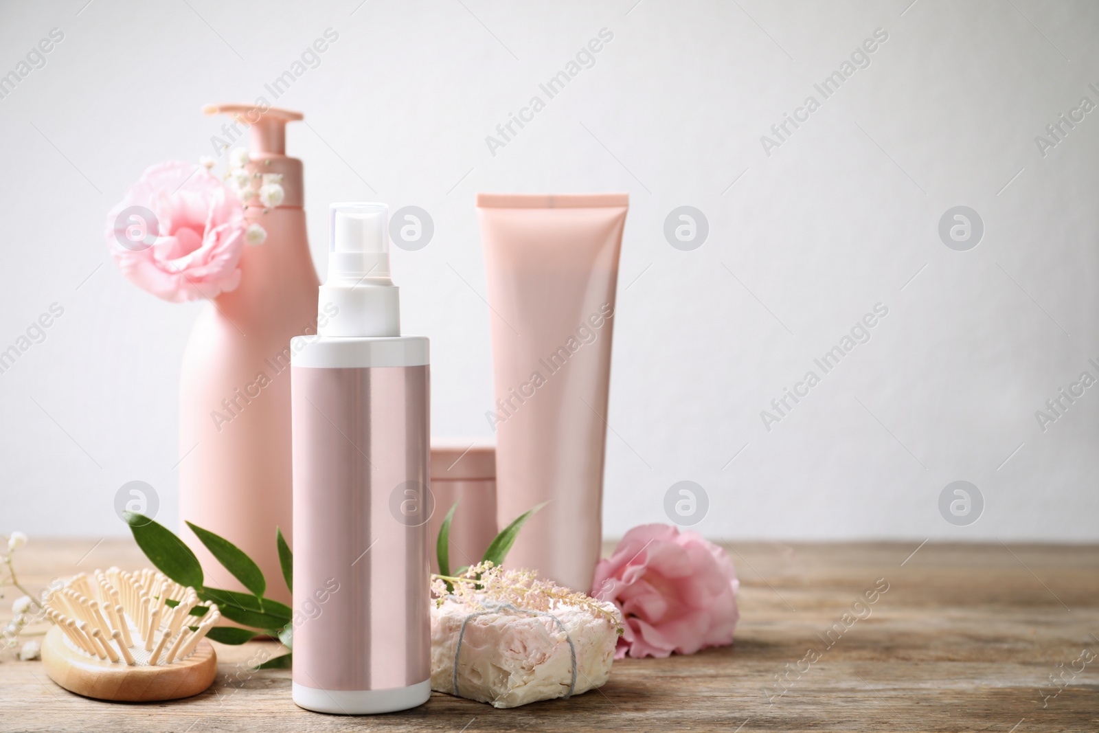 Photo of Set of hair cosmetic products, brush and flowers on wooden table against white background. Space for text