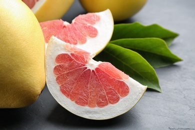 Photo of Fresh cut and whole pomelo fruits on black slate table, closeup