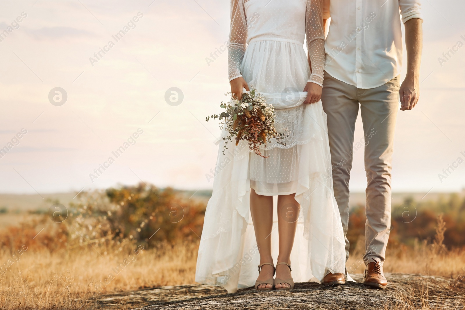 Photo of Happy newlyweds with beautiful field bouquet outdoors, closeup