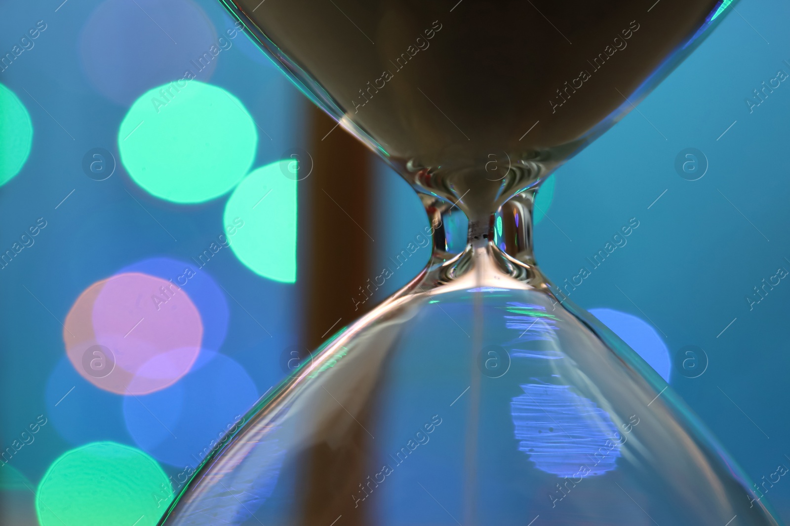 Photo of Hourglass with flowing sand against blurred lights, closeup. Christmas countdown