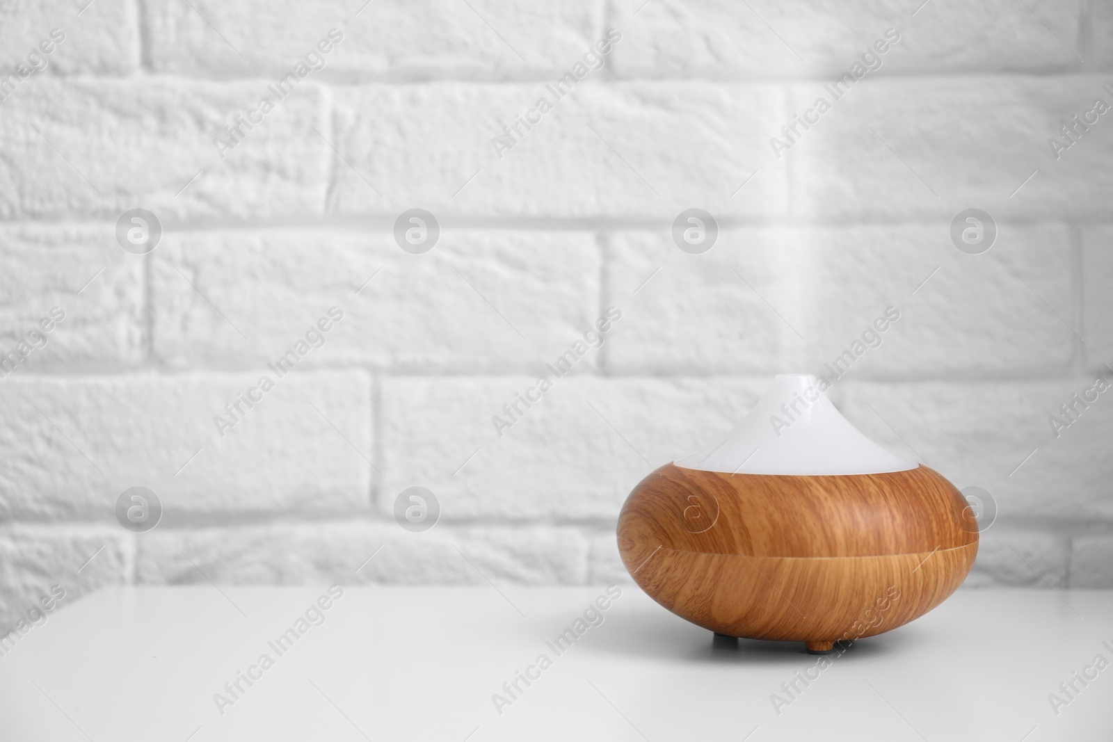 Photo of Essential oils diffuser on white table   near brick wall. Space for text