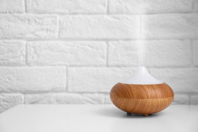 Essential oils diffuser on white table   near brick wall. Space for text