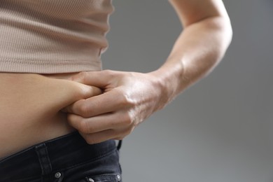 Woman touching belly fat on grey background, closeup. Overweight problem