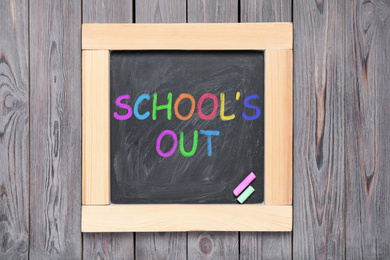 Image of Chalkboard with text SCHOOL'S OUT on grey wooden background, top view