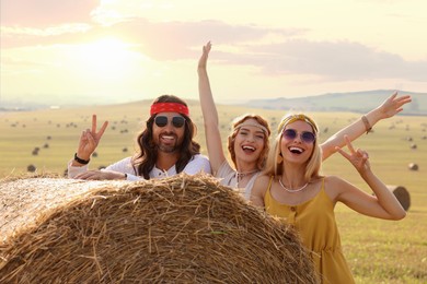 Happy hippie friends near hay bale in field