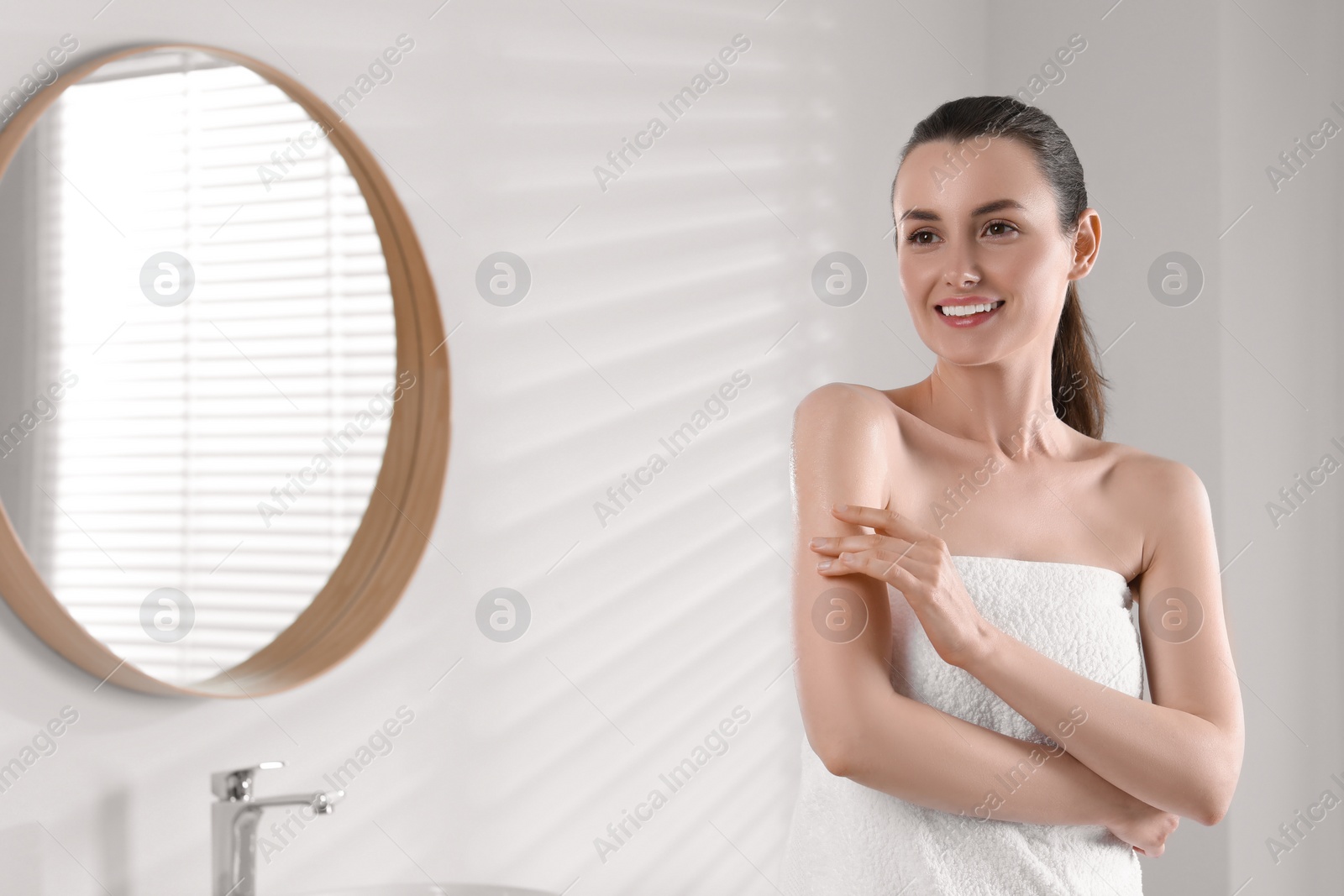 Photo of Happy woman applying body oil onto arm in bathroom, space for text