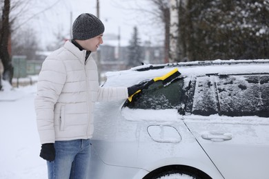 Man cleaning snow from car with brush outdoors