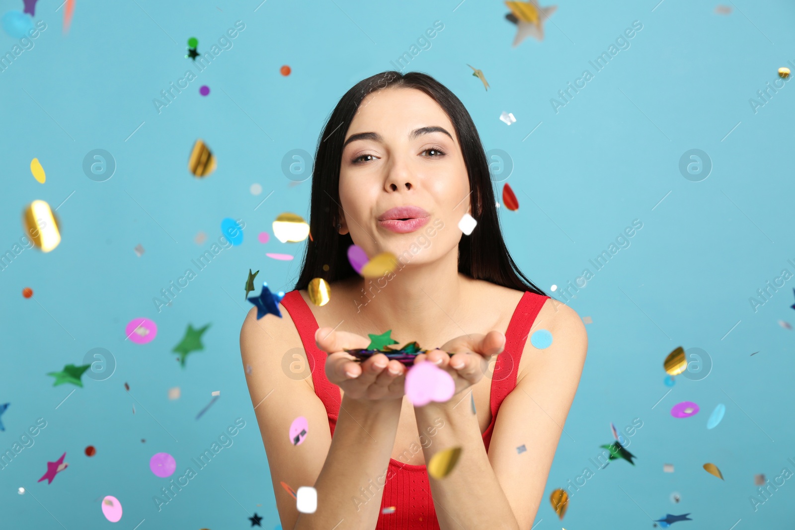 Photo of Happy woman blowing confetti on light blue background