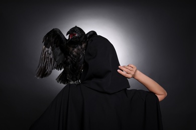 Photo of Mysterious witch with raven on black background, back view
