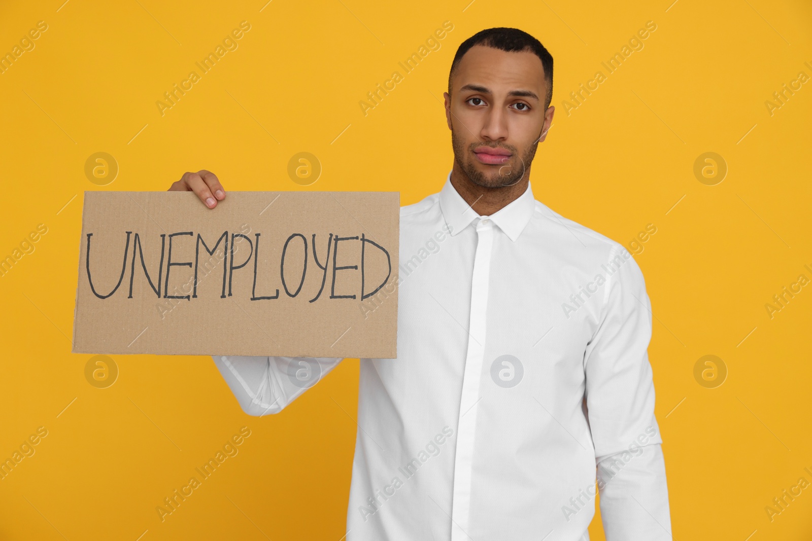 Photo of Young man holding sign with word Unemployed on yellow background