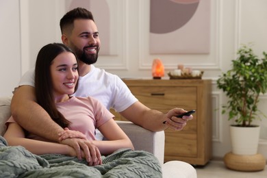 Happy young couple watching tv on sofa in living room. Space for text