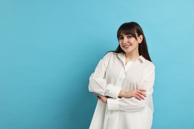 Happy woman wearing pyjama on light blue background, space for text