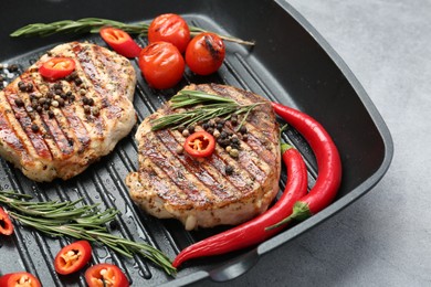 Grill pan with delicious pork steaks, spices and vegetables on grey table, closeup