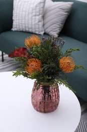 Vase with bouquet of beautiful leucospermum flowers on white coffee table in living room