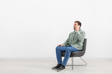 Photo of Young man talking on smartphone while sitting on chair indoors. Space for text
