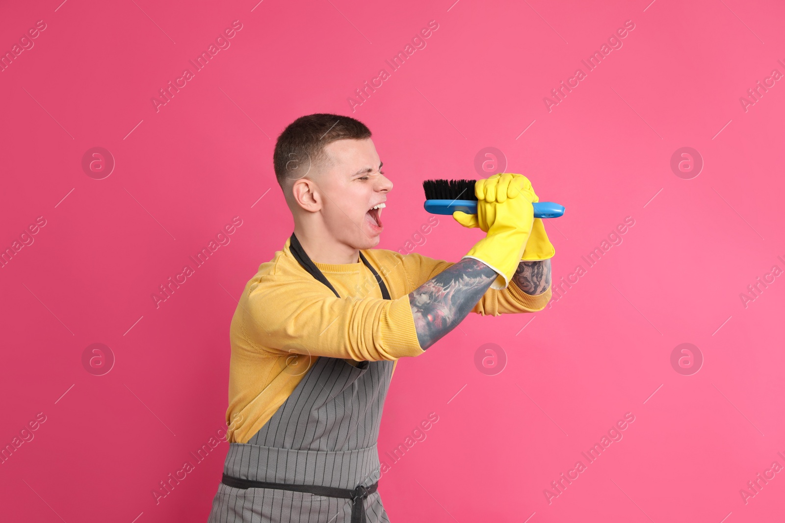 Photo of Handsome young man with brush singing on pink background