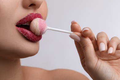 Young woman with beautiful lips covered in sugar eating lollipop on light background, closeup