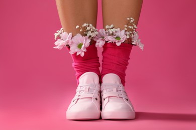 Photo of Woman with beautiful tender flowers in socks on pink background, closeup