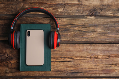 Photo of Book, modern headphones and smartphone on wooden table, flat lay. Space for text
