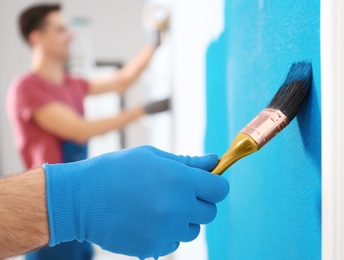 Photo of Male decorator painting wall with brush indoors, closeup