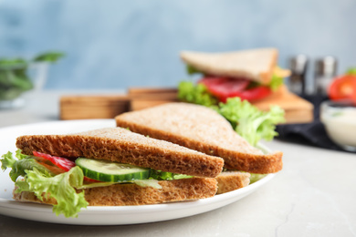 Photo of Tasty fresh sandwiches with cucumbers and sausage on light grey table, closeup