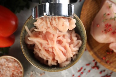 Photo of Electric meat grinder with chicken mince and products on grey table indoors, flat lay