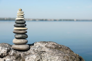 Photo of Stack of stones on rock near river, space for text. Harmony and balance concept