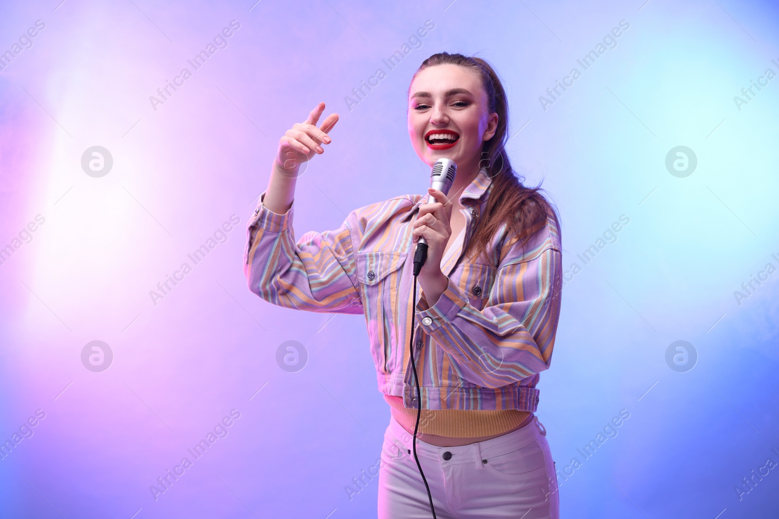 Photo of Emotional woman with microphone singing in color lights. Space for text