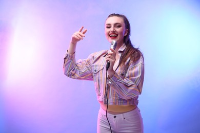 Photo of Emotional woman with microphone singing in color lights. Space for text