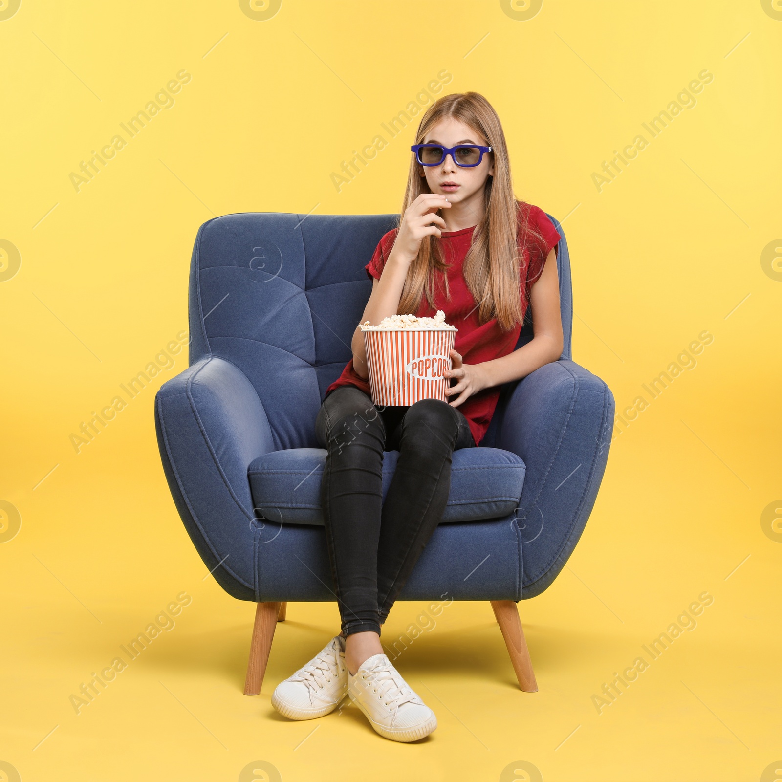 Photo of Emotional teenage girl with 3D glasses and popcorn sitting in armchair during cinema show on color background