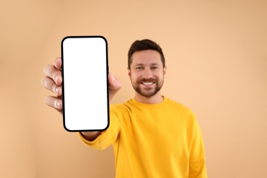 Photo of Handsome man showing smartphone in hand on light brown background, selective focus. Mockup for design