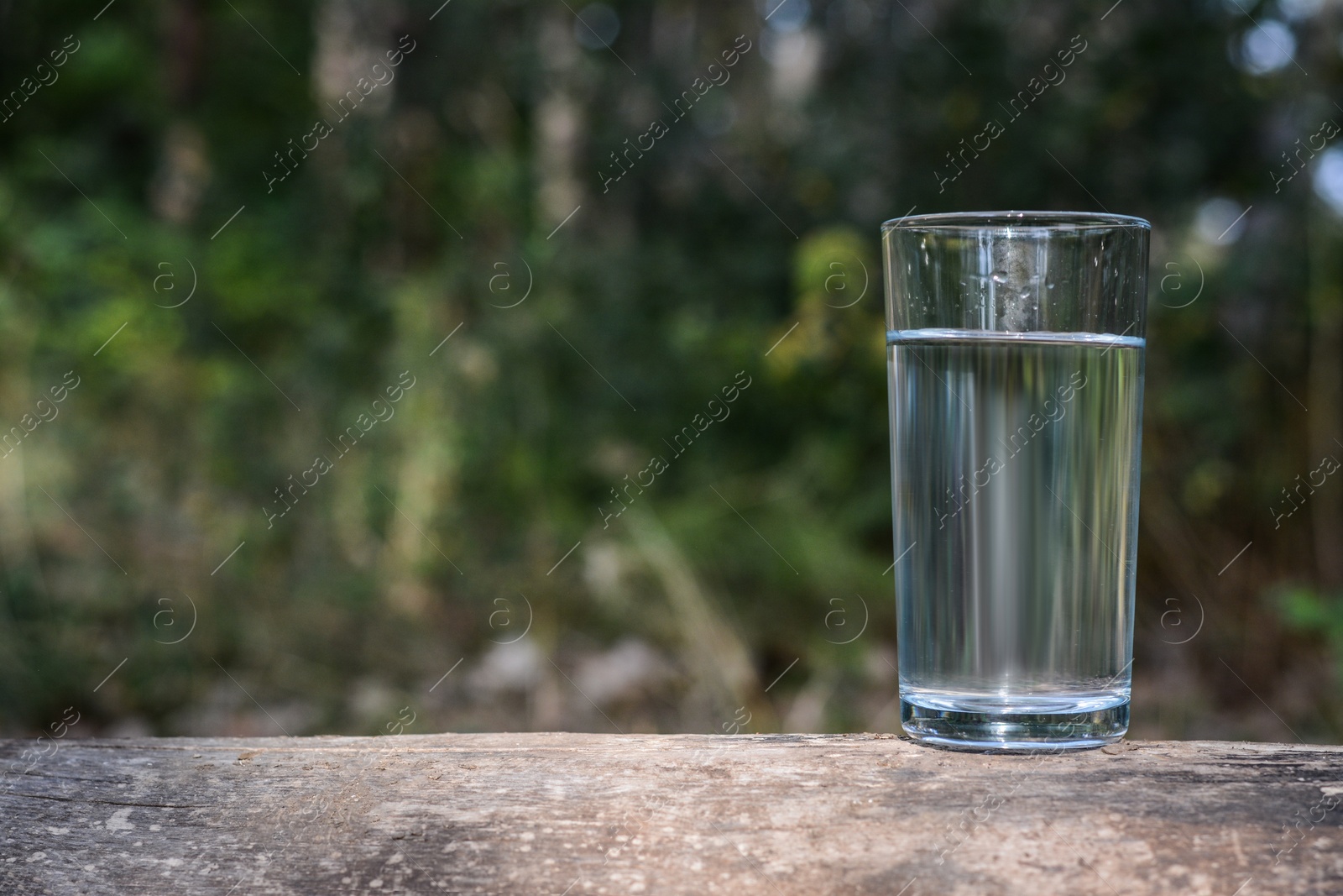 Photo of Glass of water on wooden surface outdoors, space for text