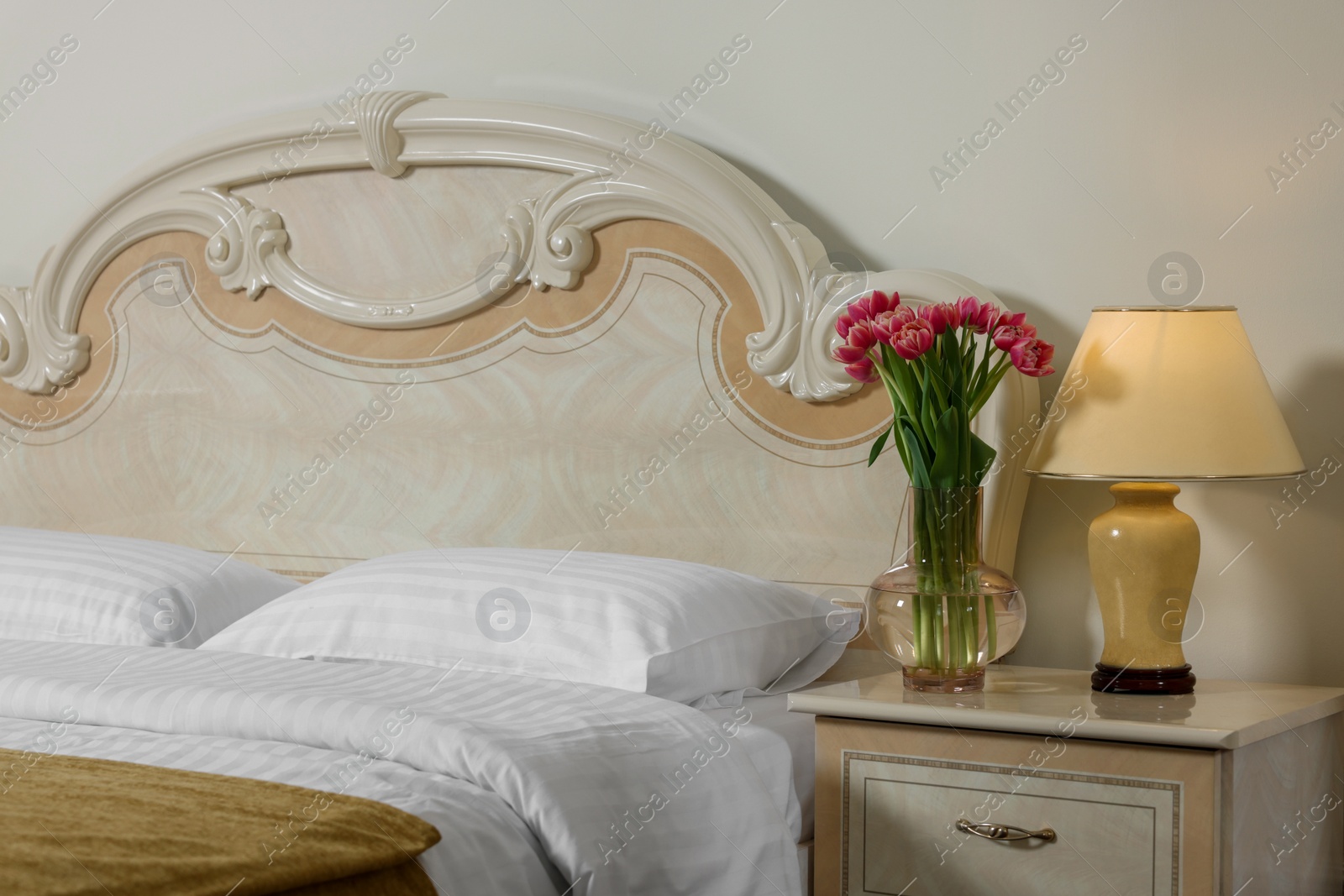 Photo of Comfortable bed and beautiful bouquet on bedside table in room. Stylish interior