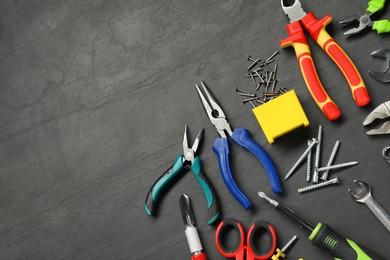 Photo of Different pliers, screwdriver, wrenches and other repair tools on black textured table, flat lay. Space for text