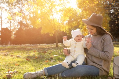 Photo of Happy mother with her baby daughter sitting on grass in autumn park, space for text