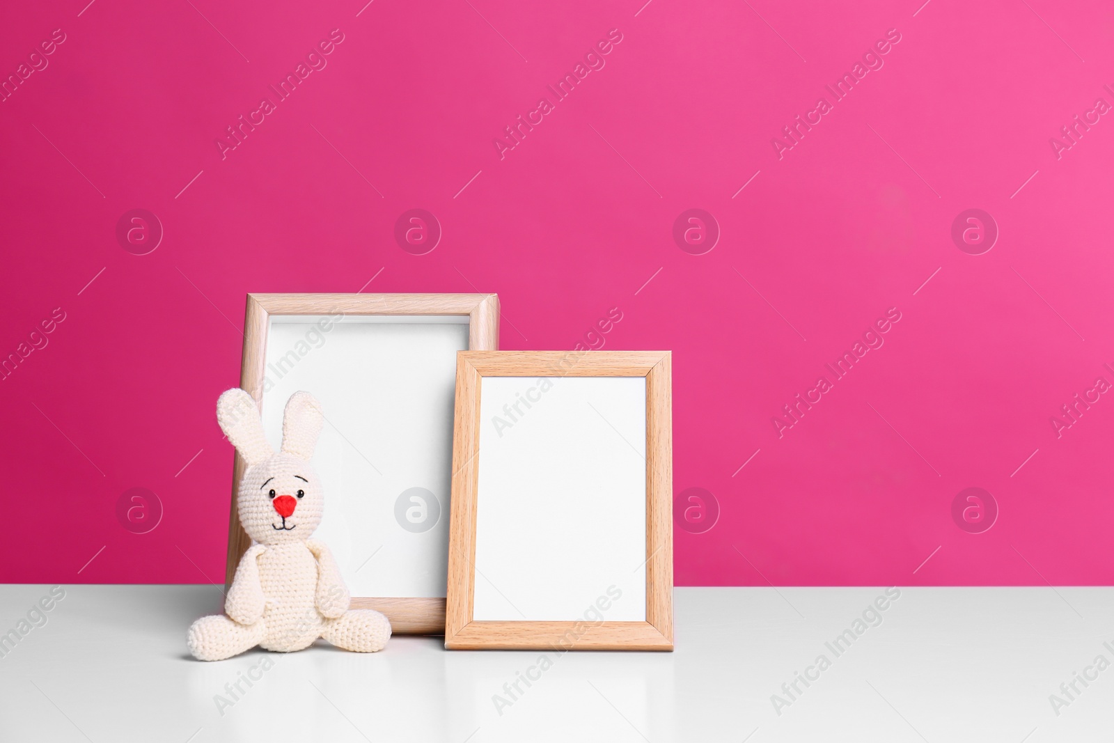 Photo of Photo frames and adorable toy bunny on table against color background, space for text. Child room elements