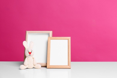 Photo of Photo frames and adorable toy bunny on table against color background, space for text. Child room elements