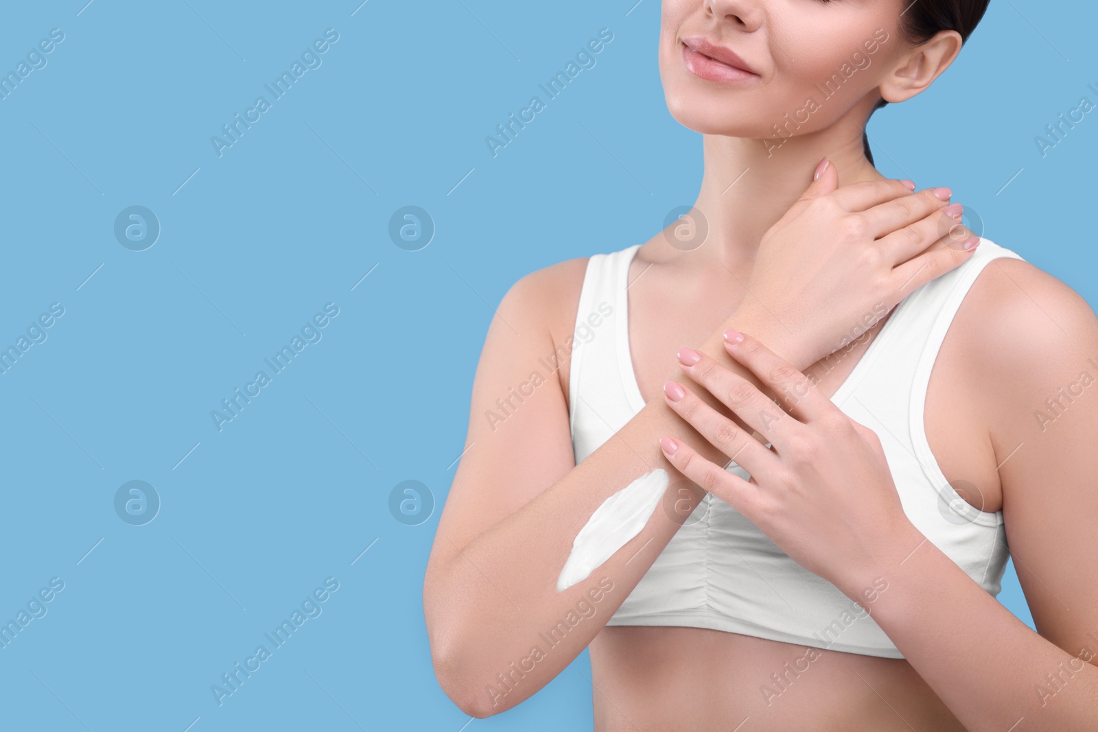 Photo of Woman with smear of body cream on her arm against light blue background, closeup. Space for text