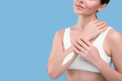 Woman with smear of body cream on her arm against light blue background, closeup. Space for text