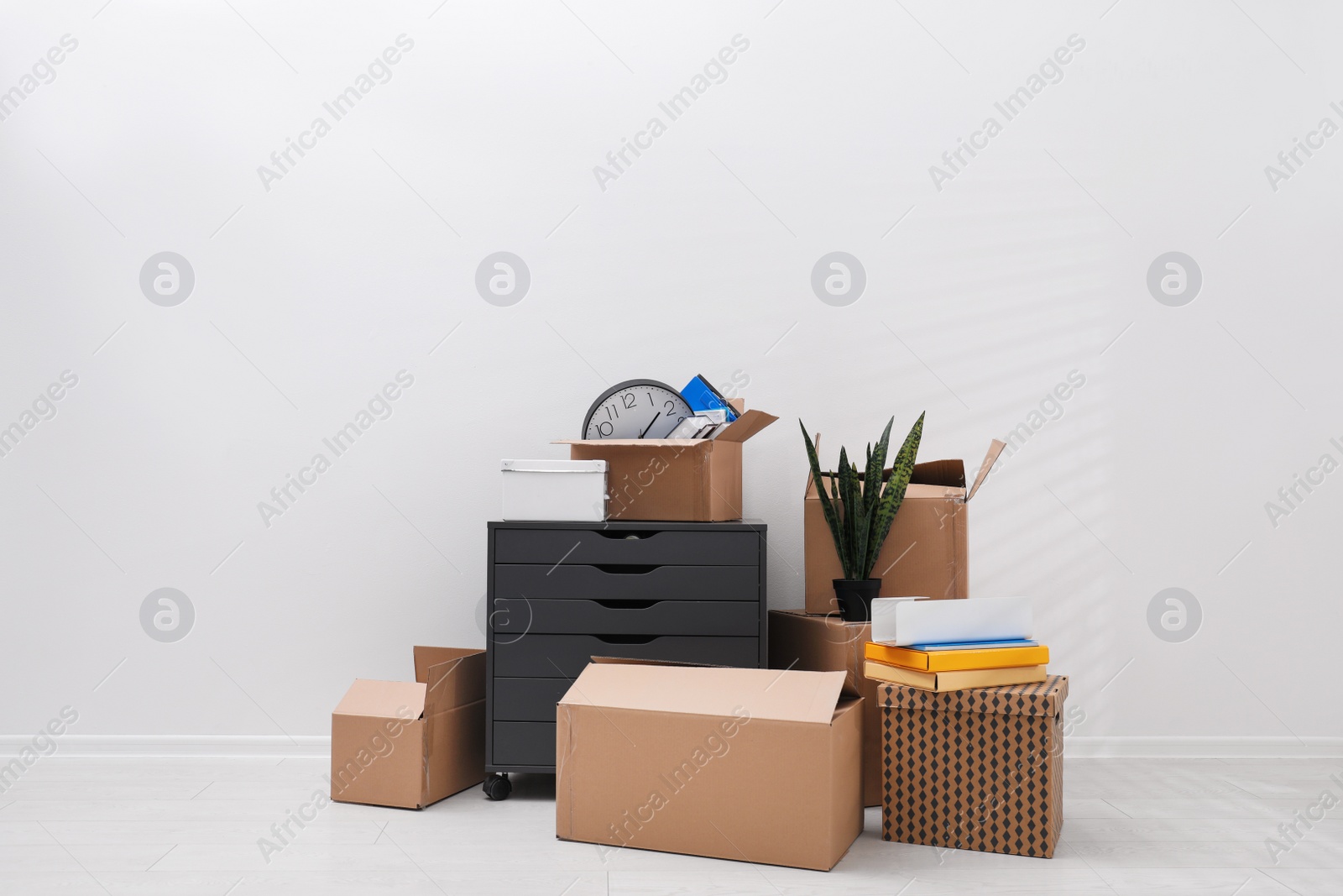 Photo of Cardboard boxes and packed belongings near white wall. Moving day