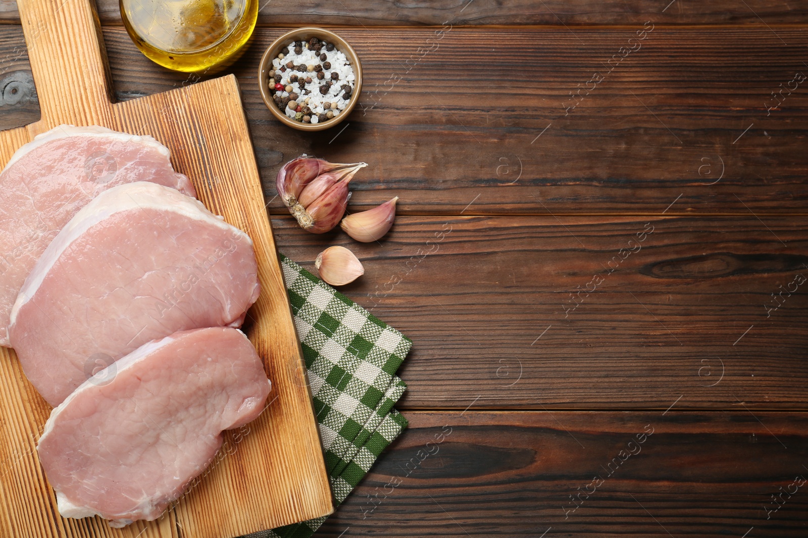 Photo of Pieces of raw pork meat, oil and spices on wooden table, flat lay. Space for text