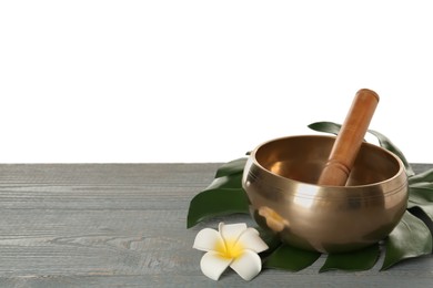 Golden singing bowl, mallet, leaf and flower on grey wooden table against white background, space for text