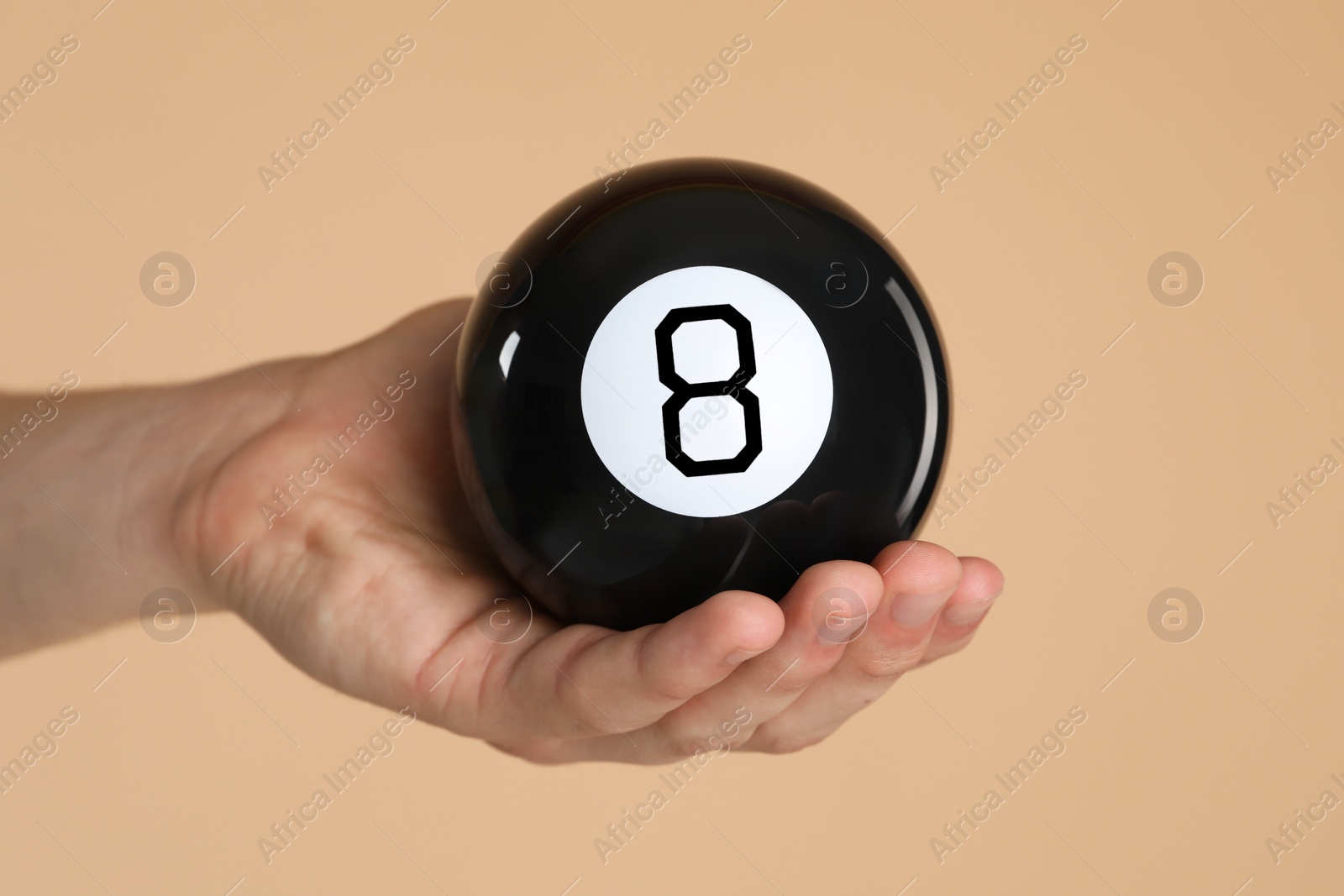 Photo of Man holding magic eight ball on light brown background, closeup