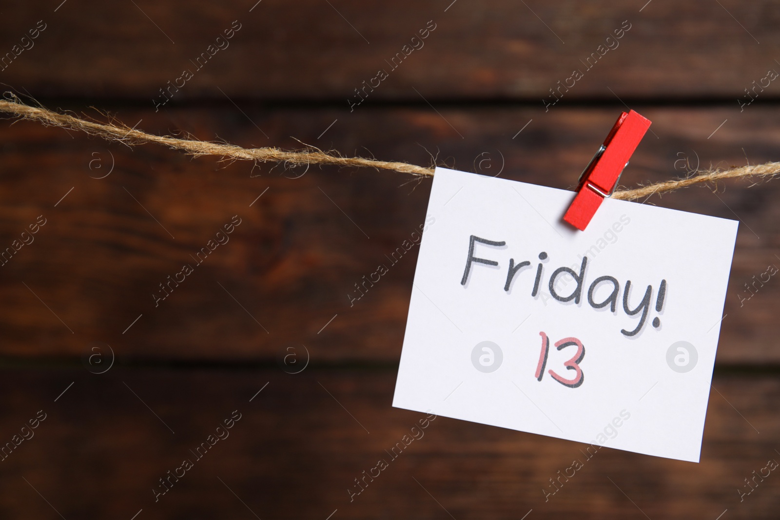 Photo of Paper note with phrase Friday! 13 hanging on twine against wooden background, space for text. Bad luck superstition